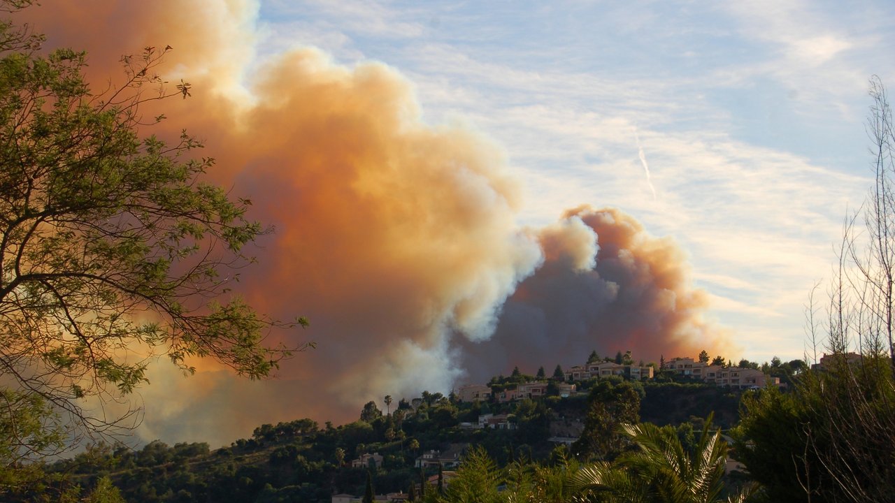 Image description: Forest and bush fires raging behind a hill in the south of France. Giant smoke clouds are going up into the sky next to the living area of the french south. Image description: Forest and bush fires raging behind a hill in the south of France. Giant smoke clouds are going up into the sky next to the living area of the french south.