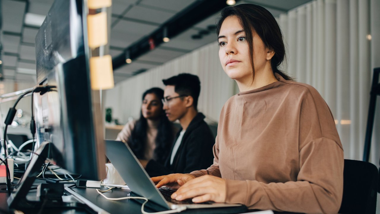 Female software engineer is programming while sitting at a desk in a large office space.