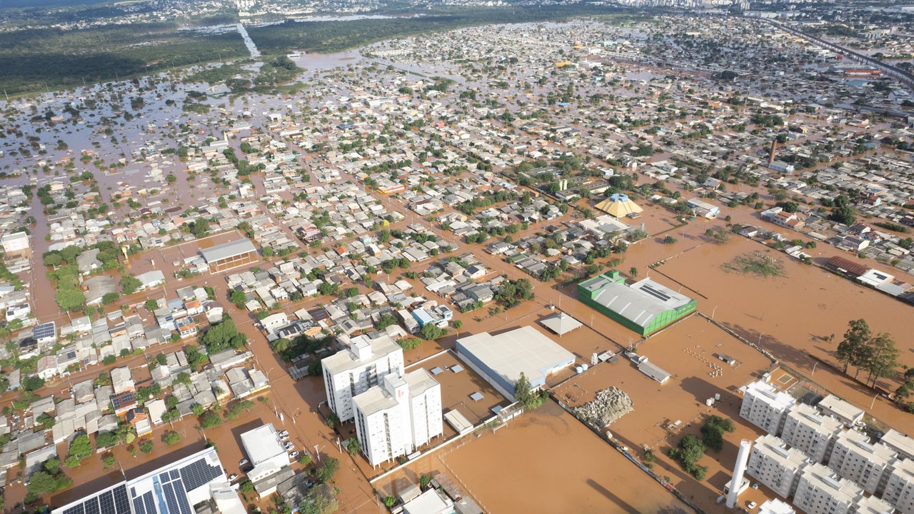 Aerial view of a flooded urban area with submerged houses, roads, and buildings, surrounded by hills in the background.